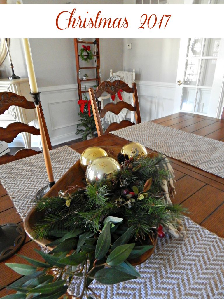 A dough bowl filled with greenery and shiny gold Christmas ornaments for a simple centerpiece.